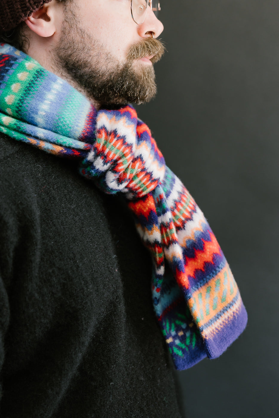 multicolored, patterned wool scarf with a purple base on a bearded man with a chocolate beanie and balck sweater, close up side view