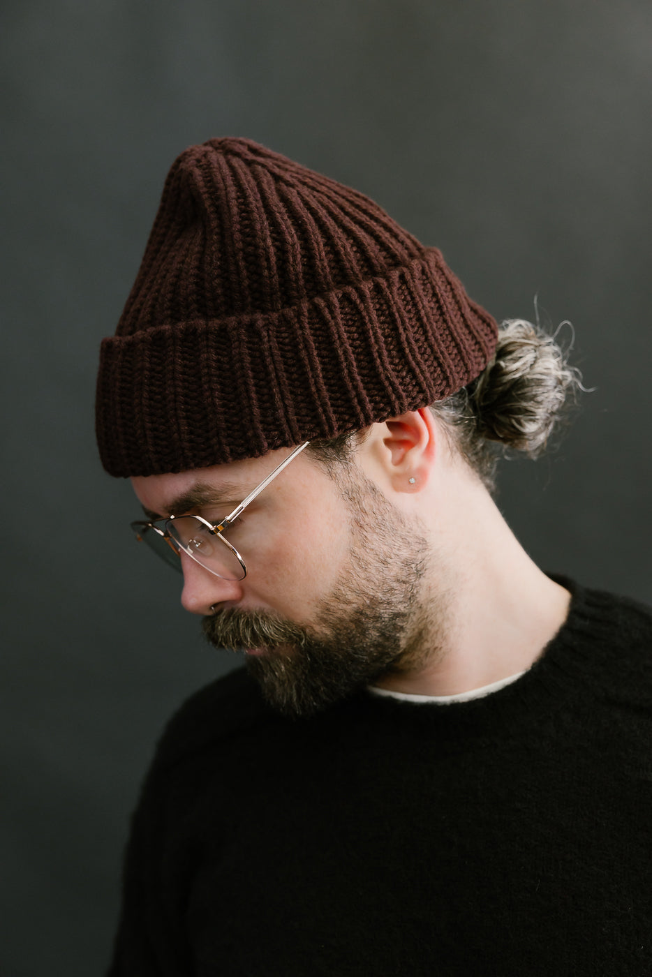 Man wearing a brown beanie and glasses against a dark background