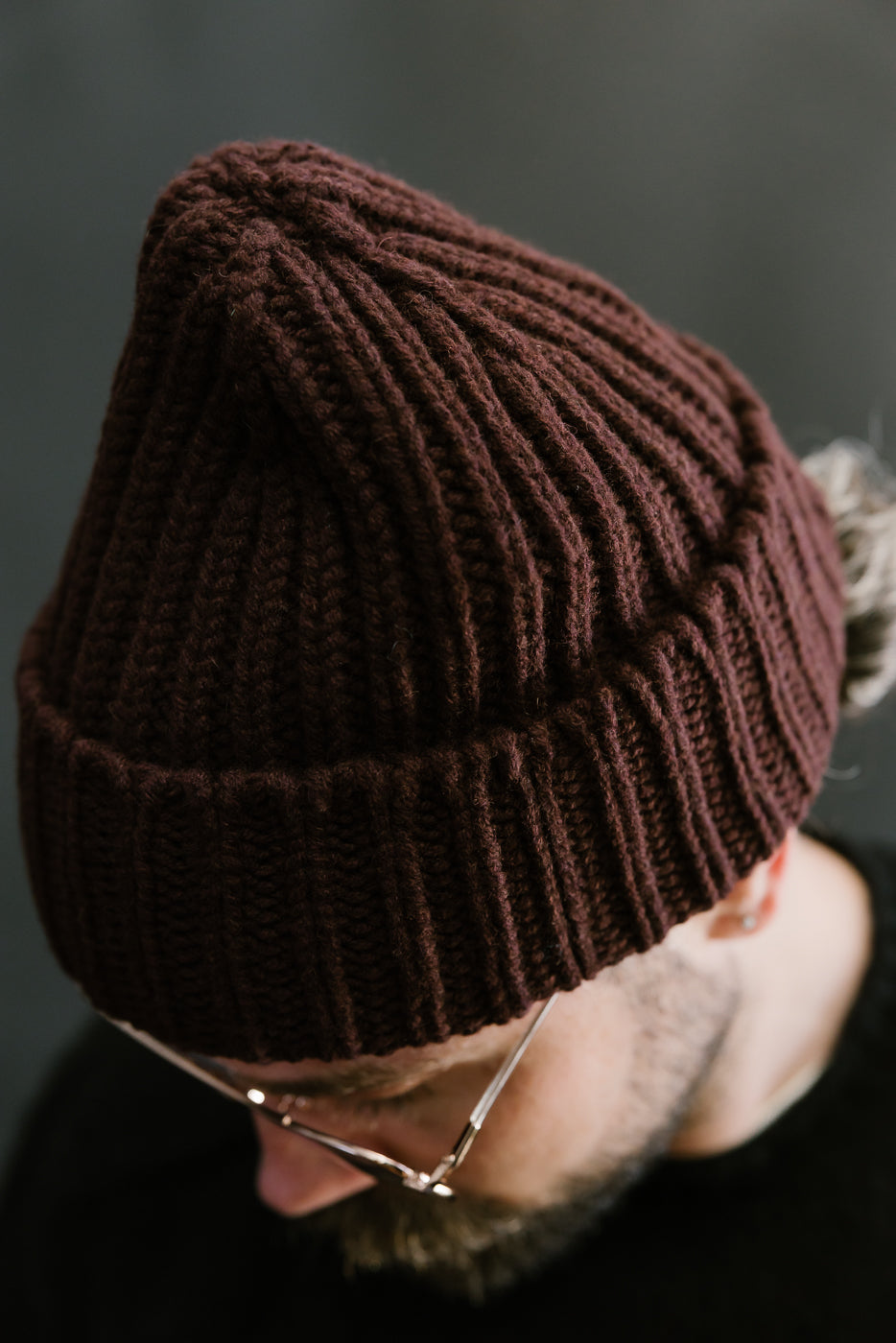 Brown knit beanie worn by a person against a dark background
