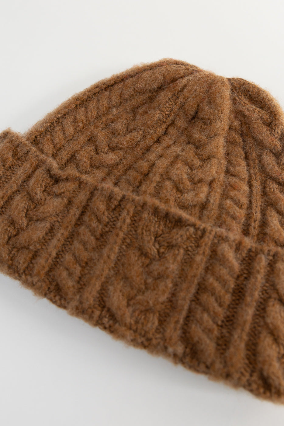 Close-up of brown cable knit beanie hat, showing side detail and fuzzy wool texture