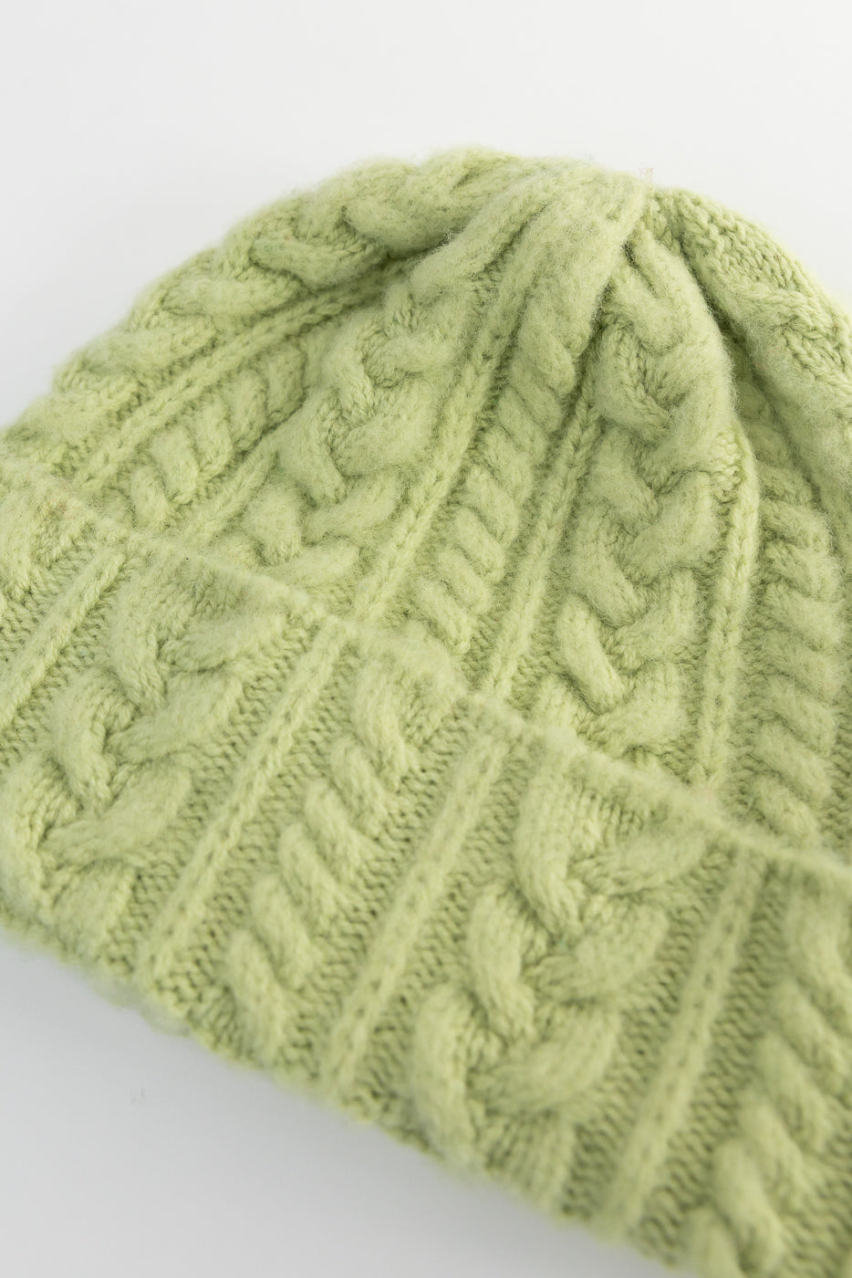 Close-up of soft green cable knit beanie, showing detailed front fabric texture.