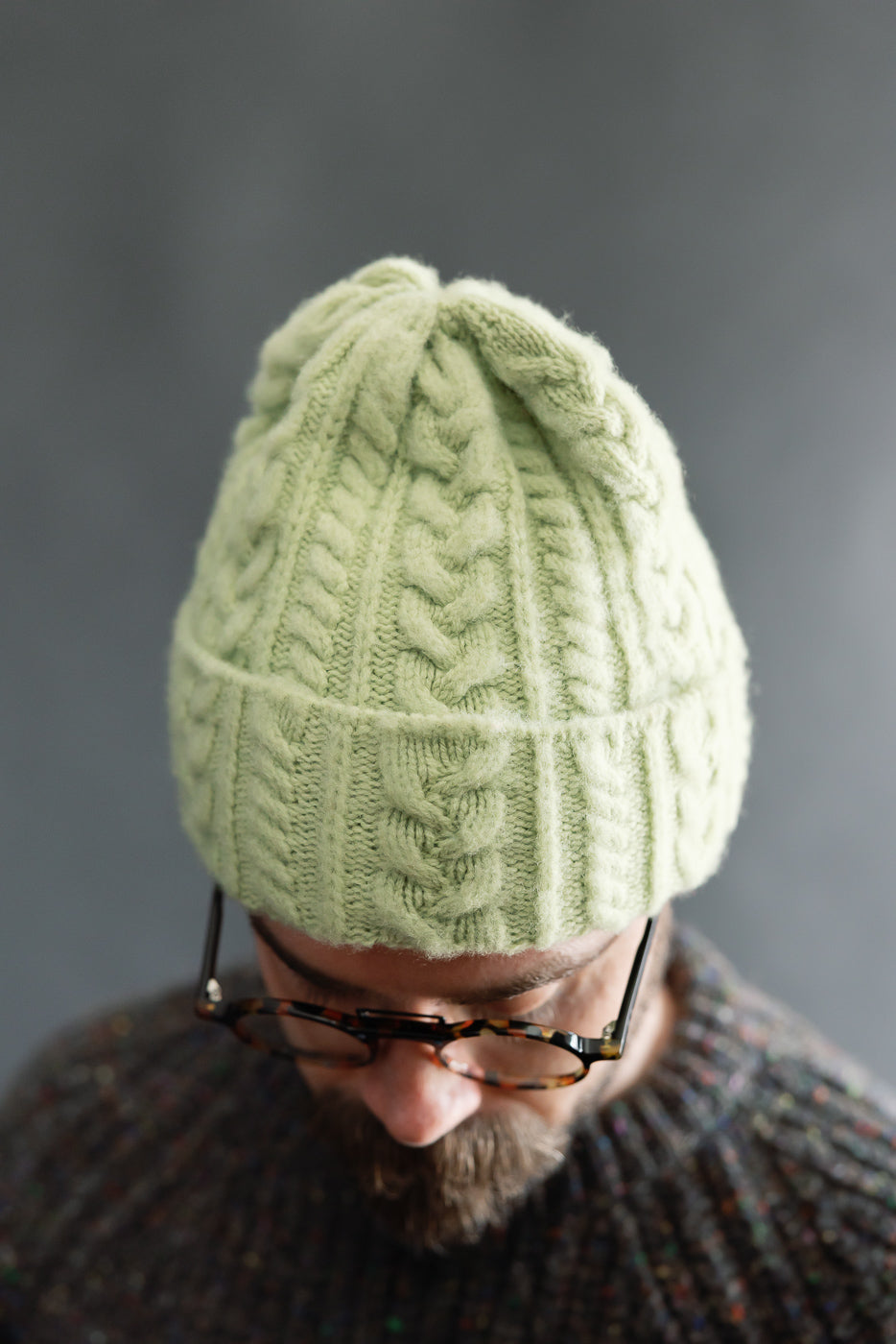 Close-up front view of soft green cable knit beanie on male model, 5'9