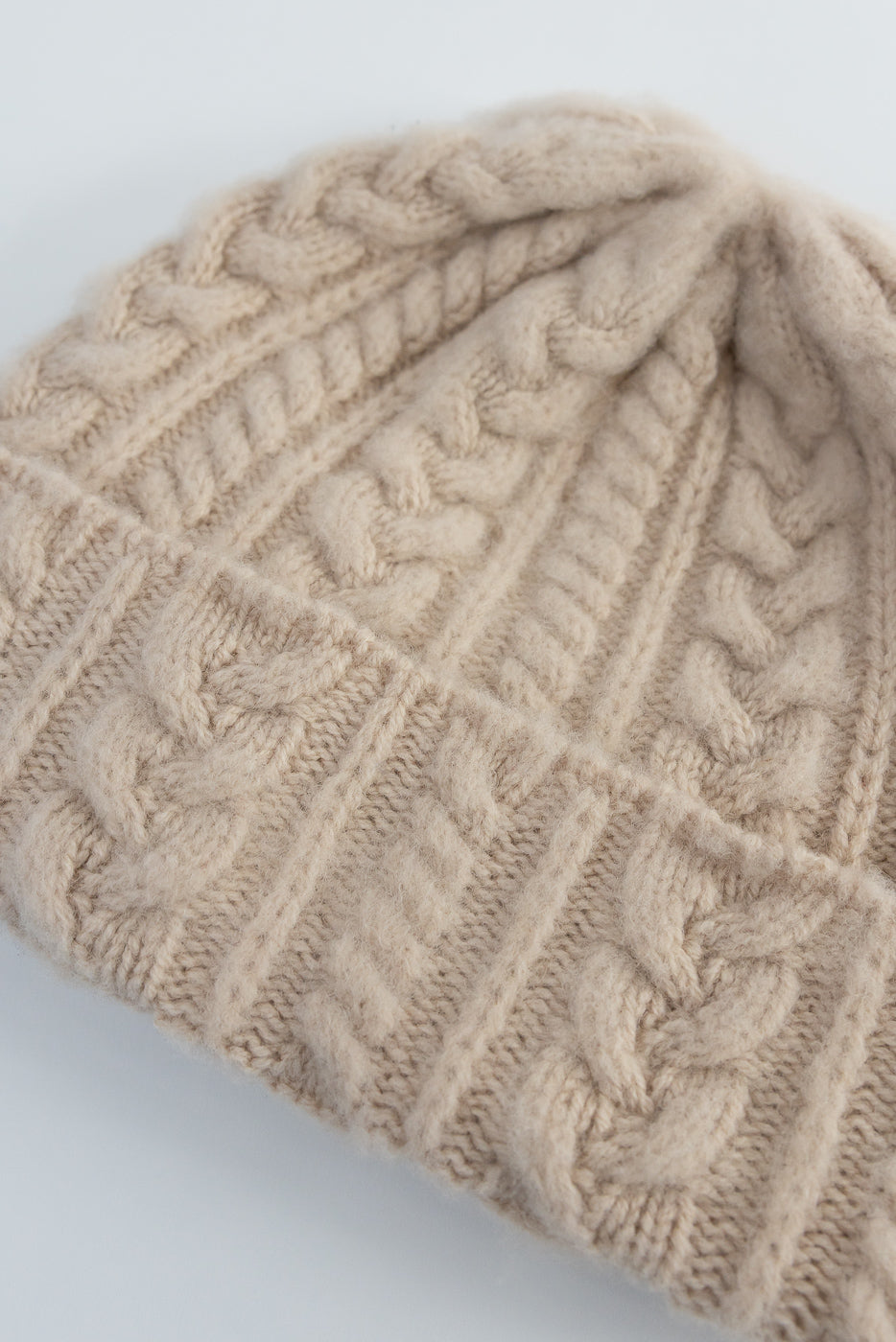 Close-up of soft oatmilk cable knit beanie hat, showing front texture and fabric detail.