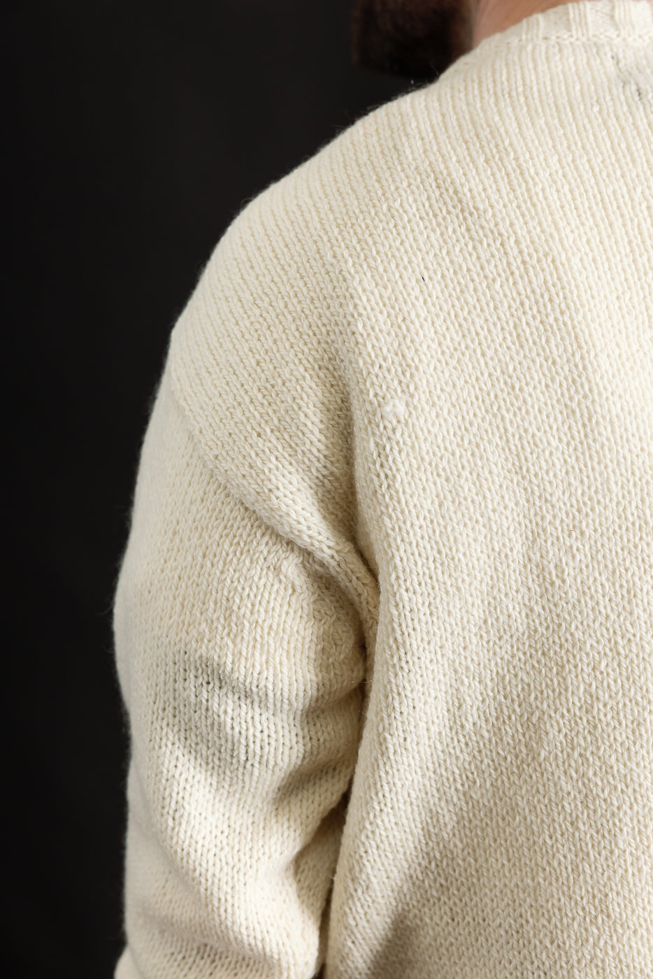 Close-up of male model’s back right shoulder wearing cream knit sweater, showing knit texture and raglan sleeve detail, model is 5'9