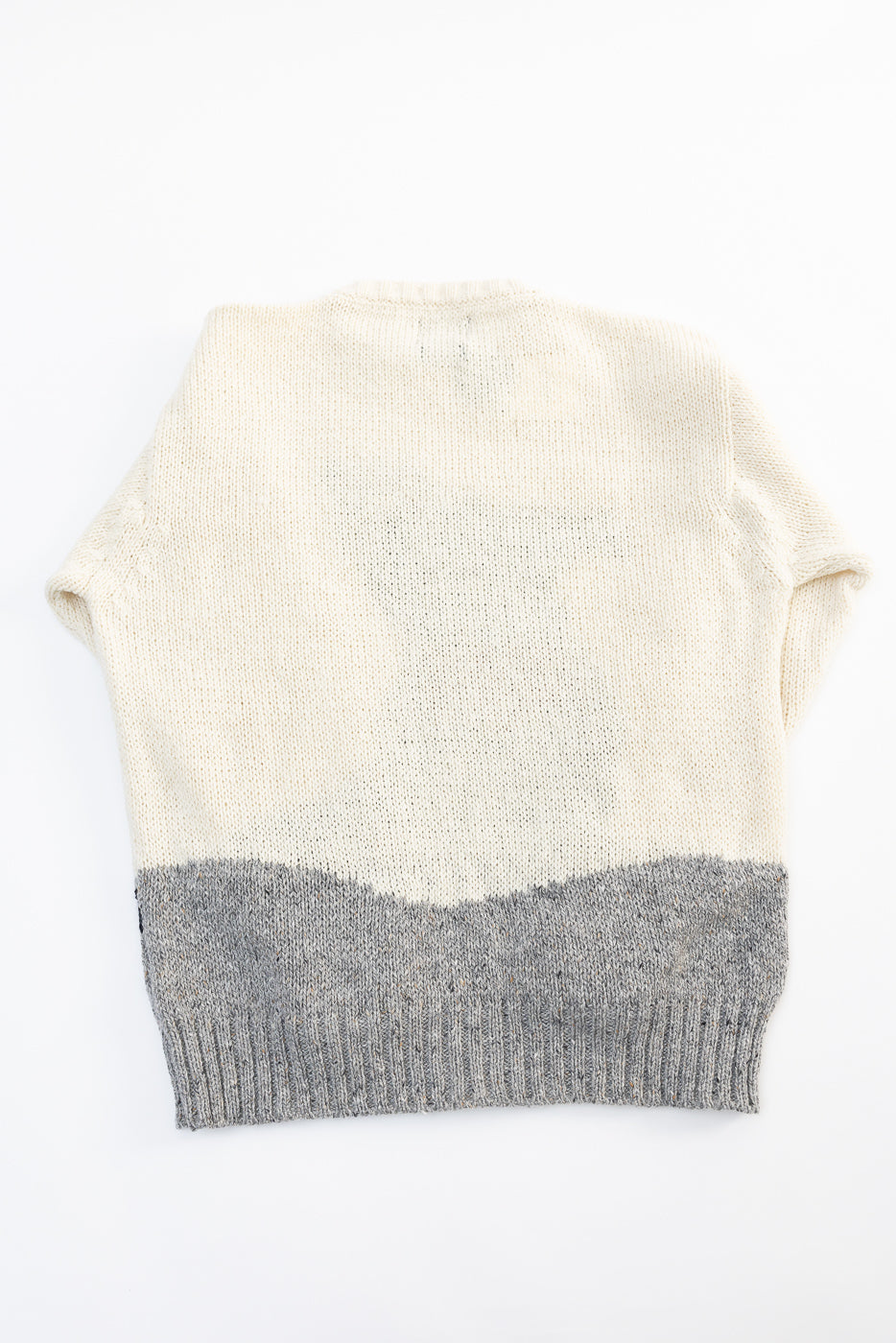 Flat lay of Howlin' knit sweater, back view, showing cream and grey color block and ribbed hem.