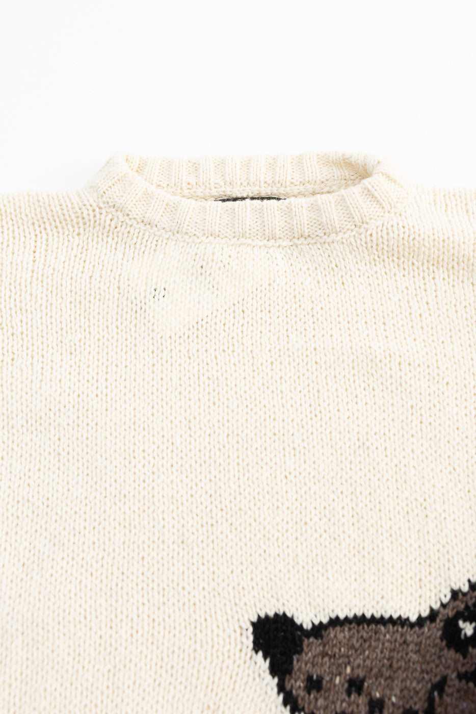 Close-up front of ecru knit sweater showing ribbed collar, fabric texture, partial graphic
