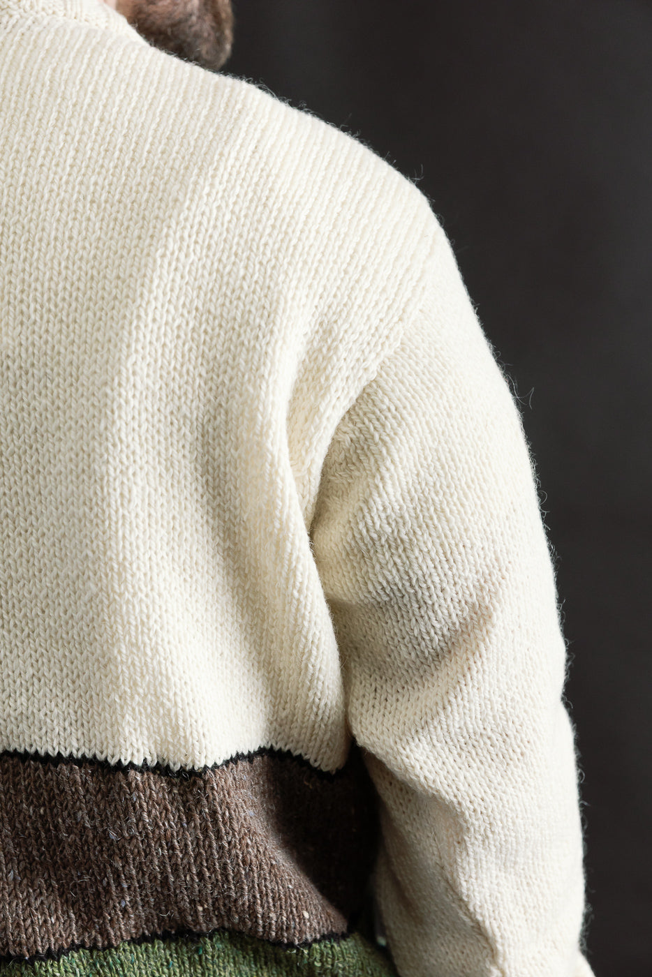 Close-up of back right shoulder on men's cream knit sweater with brown and green color block, worn by male model 5'9