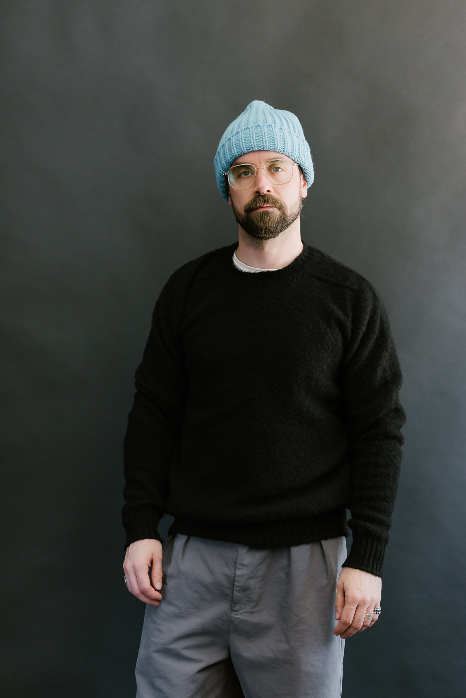 Man wearing a black sweater and blue beanie against a dark background
