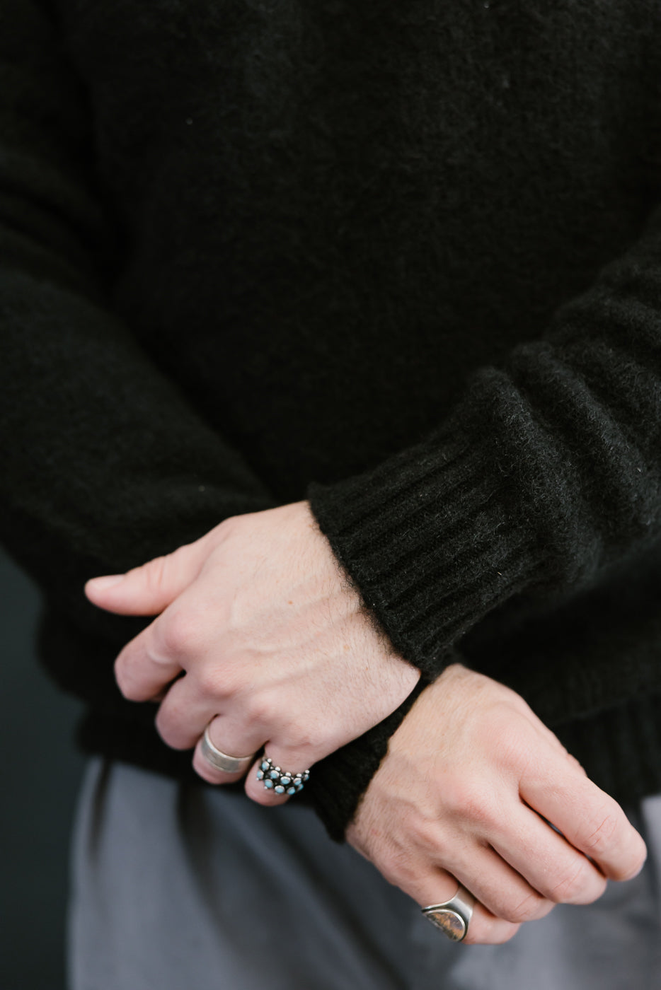 Close-up of hands wearing rings with a dark sweater background
