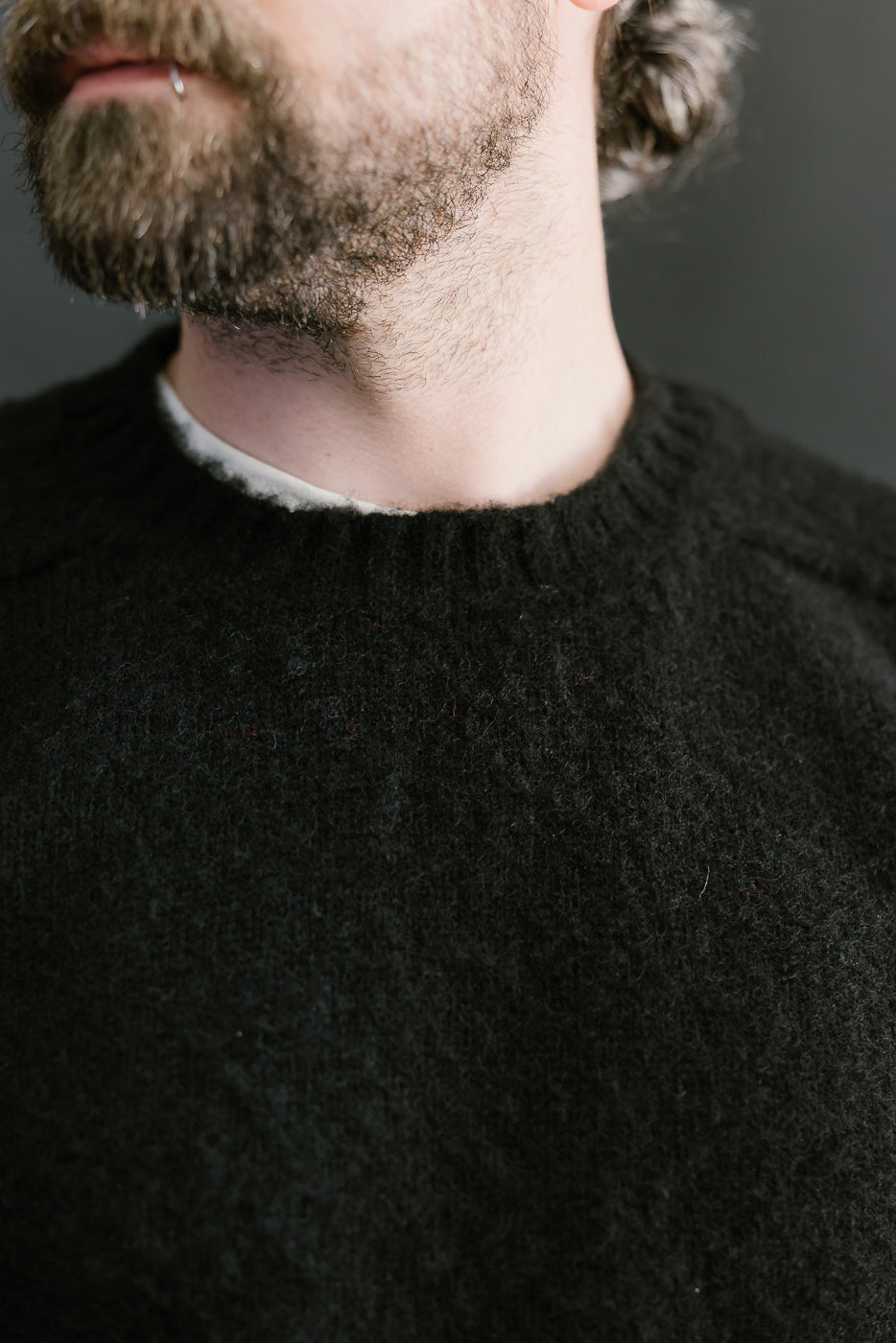 Close-up of a person wearing a black sweater with a neutral background