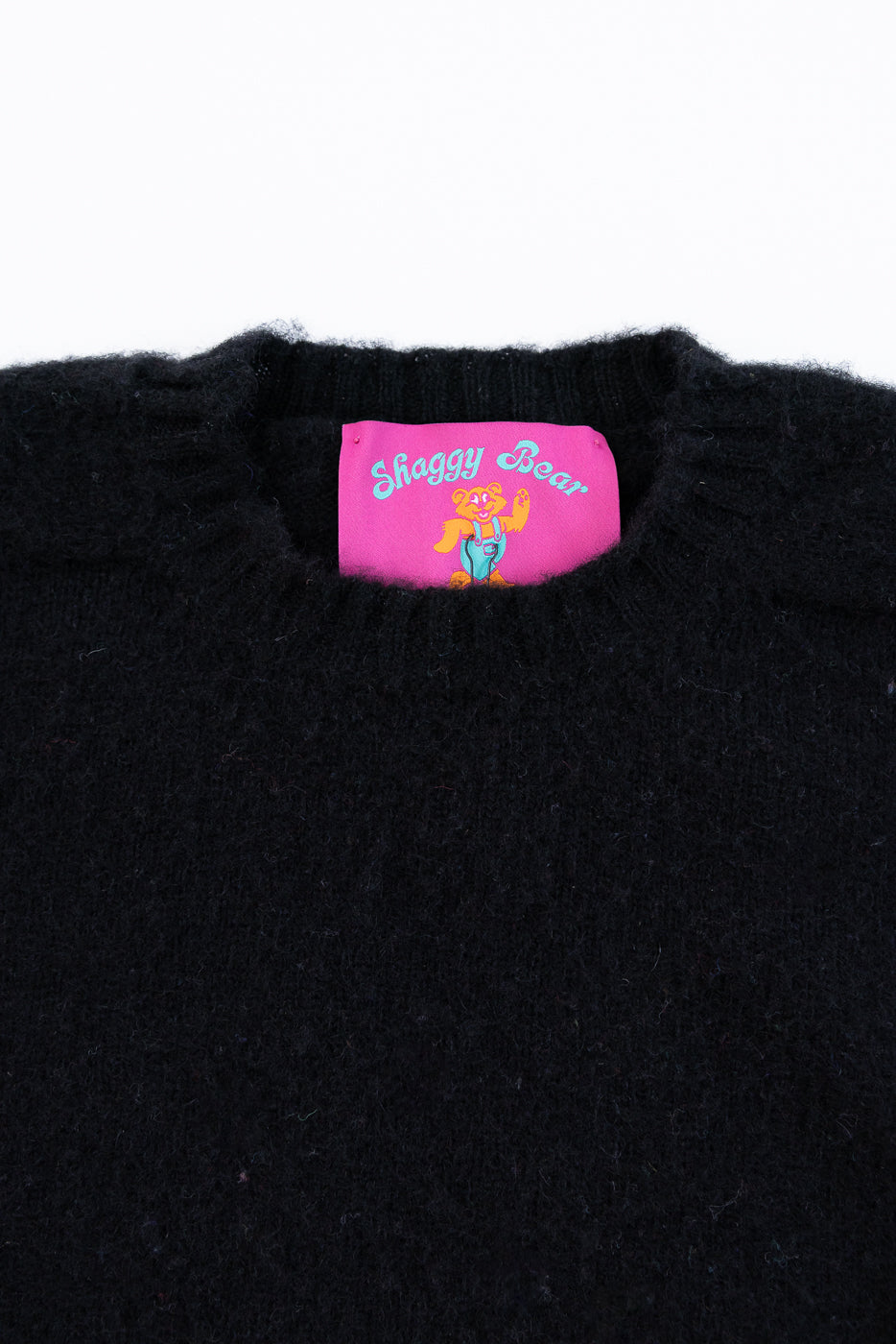 Black sweater with a pink label featuring 'Shaggy Bear' on a white background