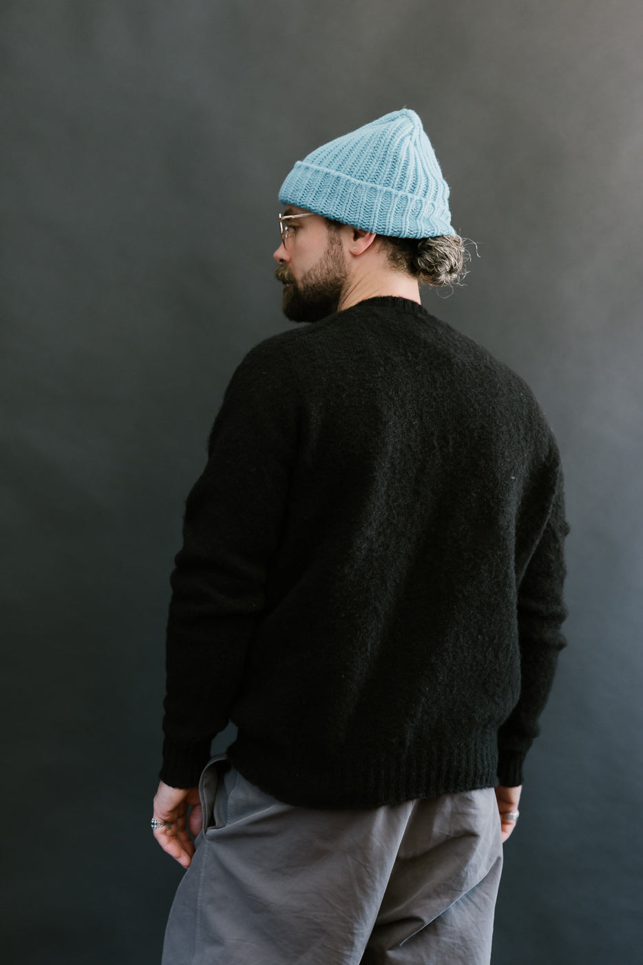 Man wearing a black sweater and light blue beanie against a dark background