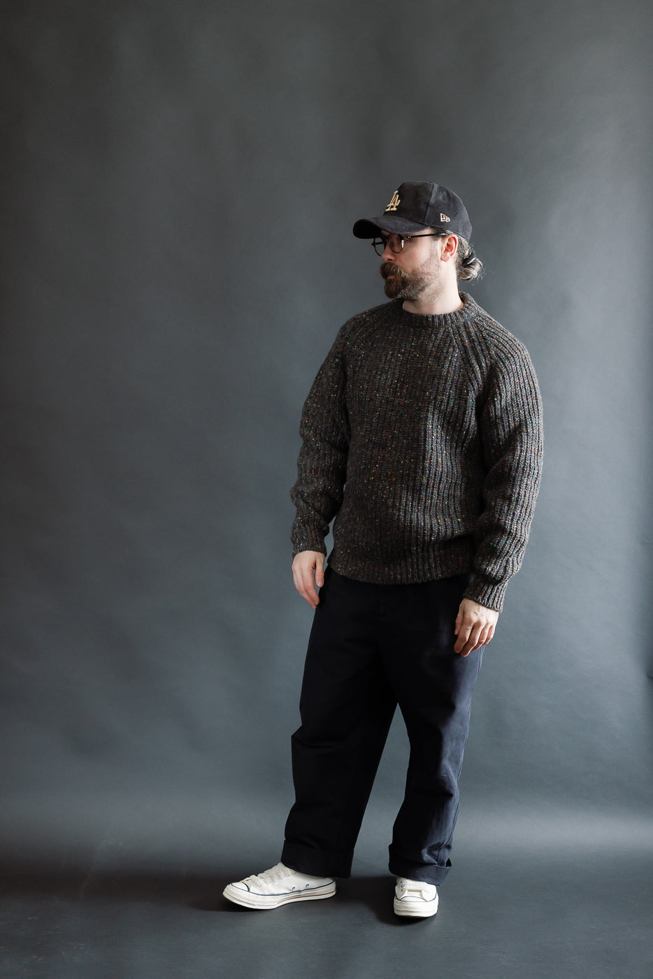 Male model 5'9 165lbs athletic build in full body front view wearing Howlin Taste of the Future pullover sweater, dark pants, and white sneakers, Dant contemporary casual apparel