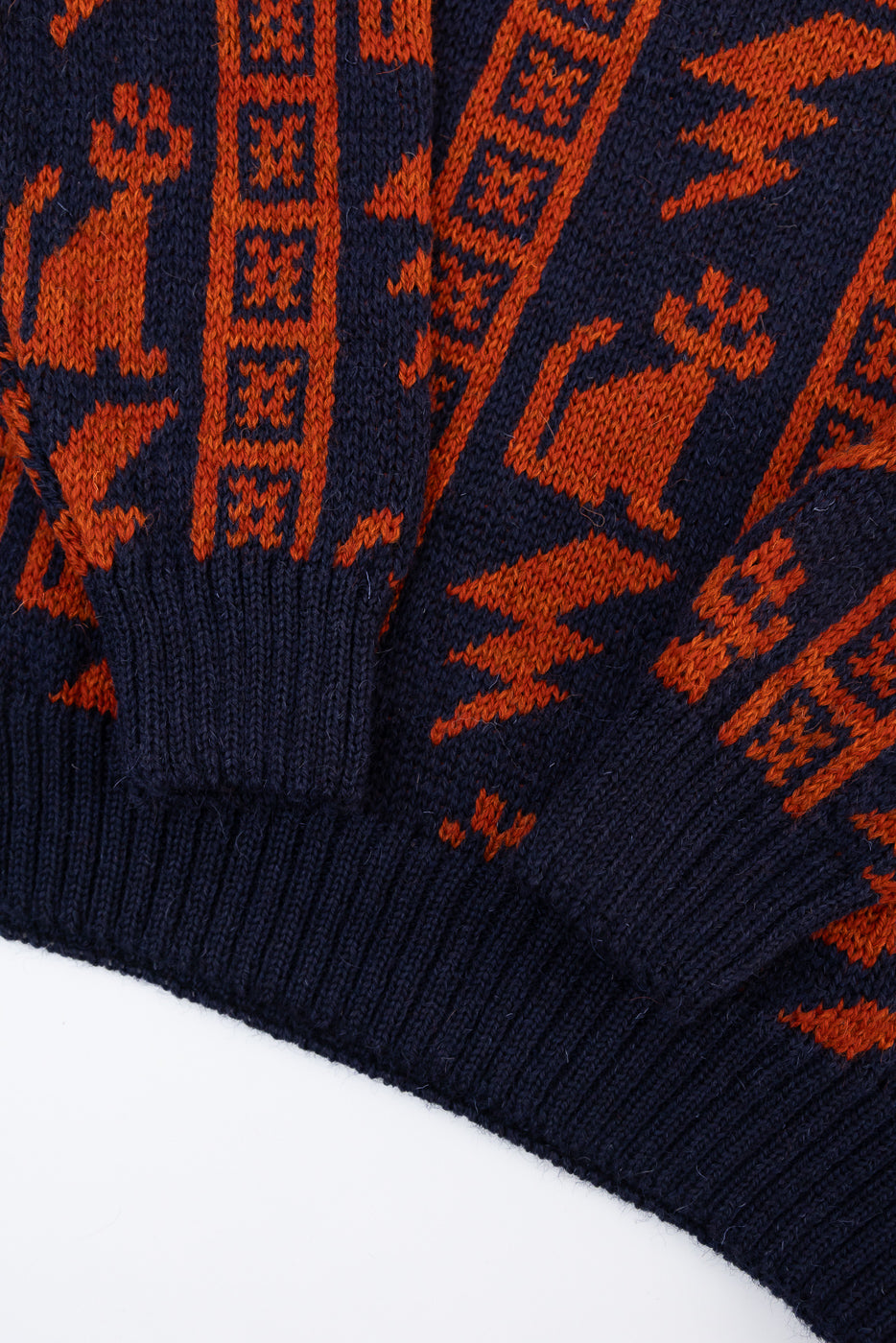 Close-up of navy knit sweater hem and cuff with orange thunder cat pattern and ribbed texture