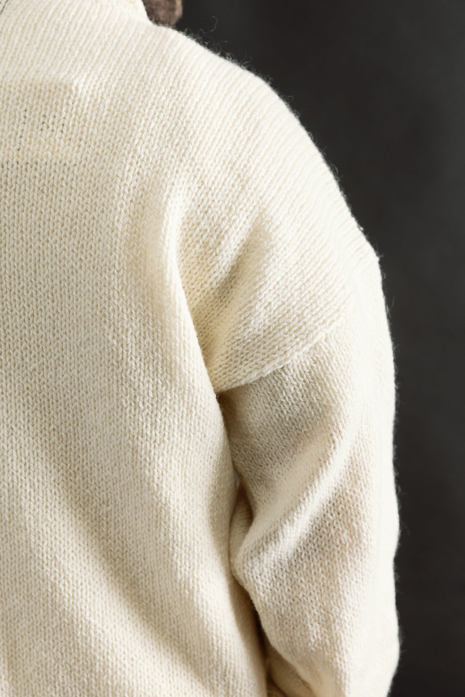 Close-up of male model’s left shoulder and upper sleeve in ecru knit sweater, showing fabric texture