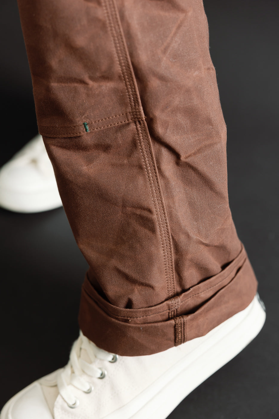 Close-up of the bottom hem and cuff of brown trousers worn by a male model.