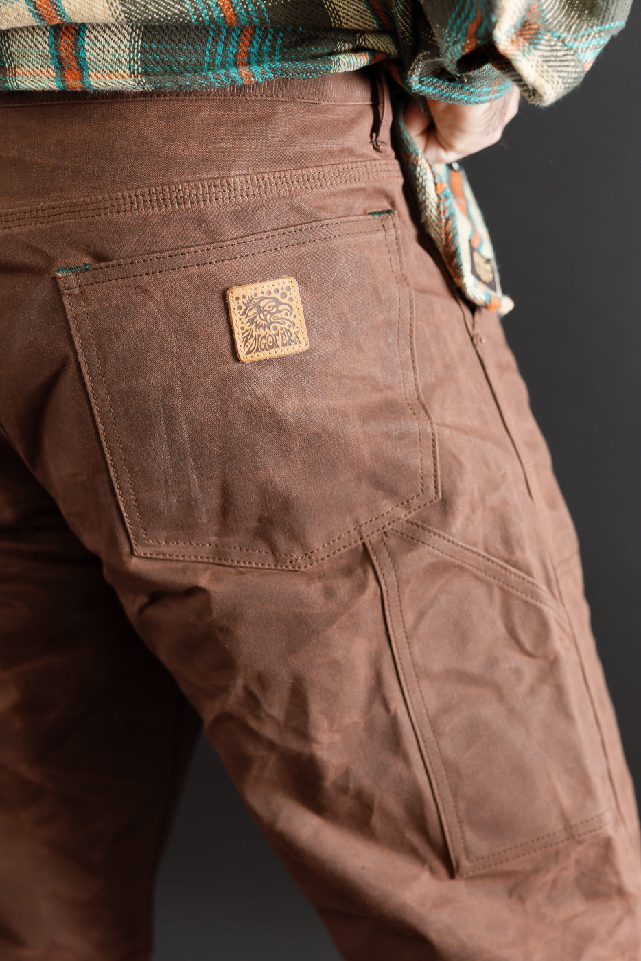 Close-up back view of brown canvas work pants showing rear pocket and leather patch detail.