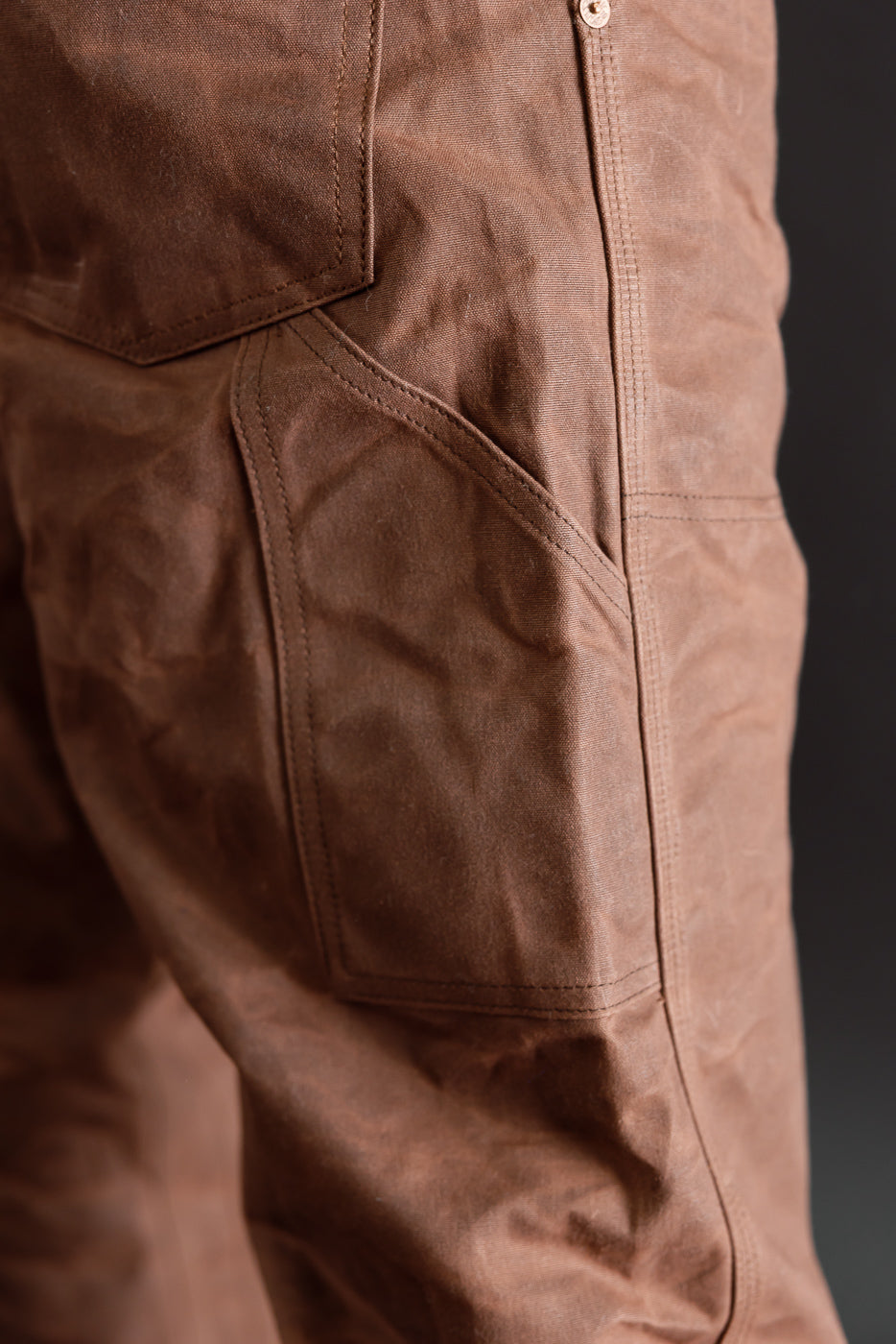 Close-up of the right side pocket on brown canvas trousers worn by a male model.
