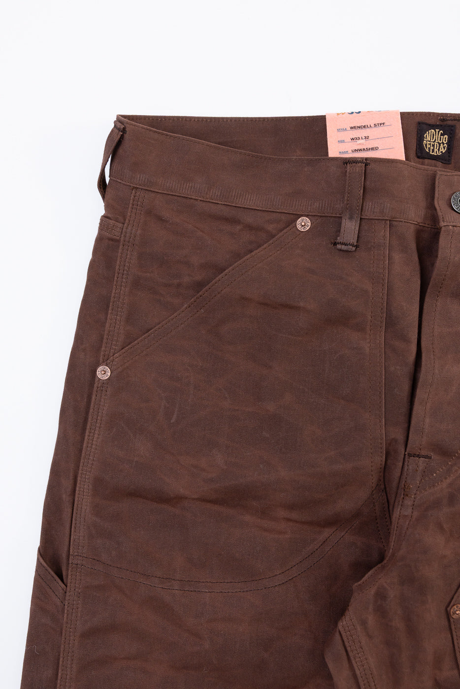 Flat lay close-up of the front right pocket and waistband of brown unwashed trousers.