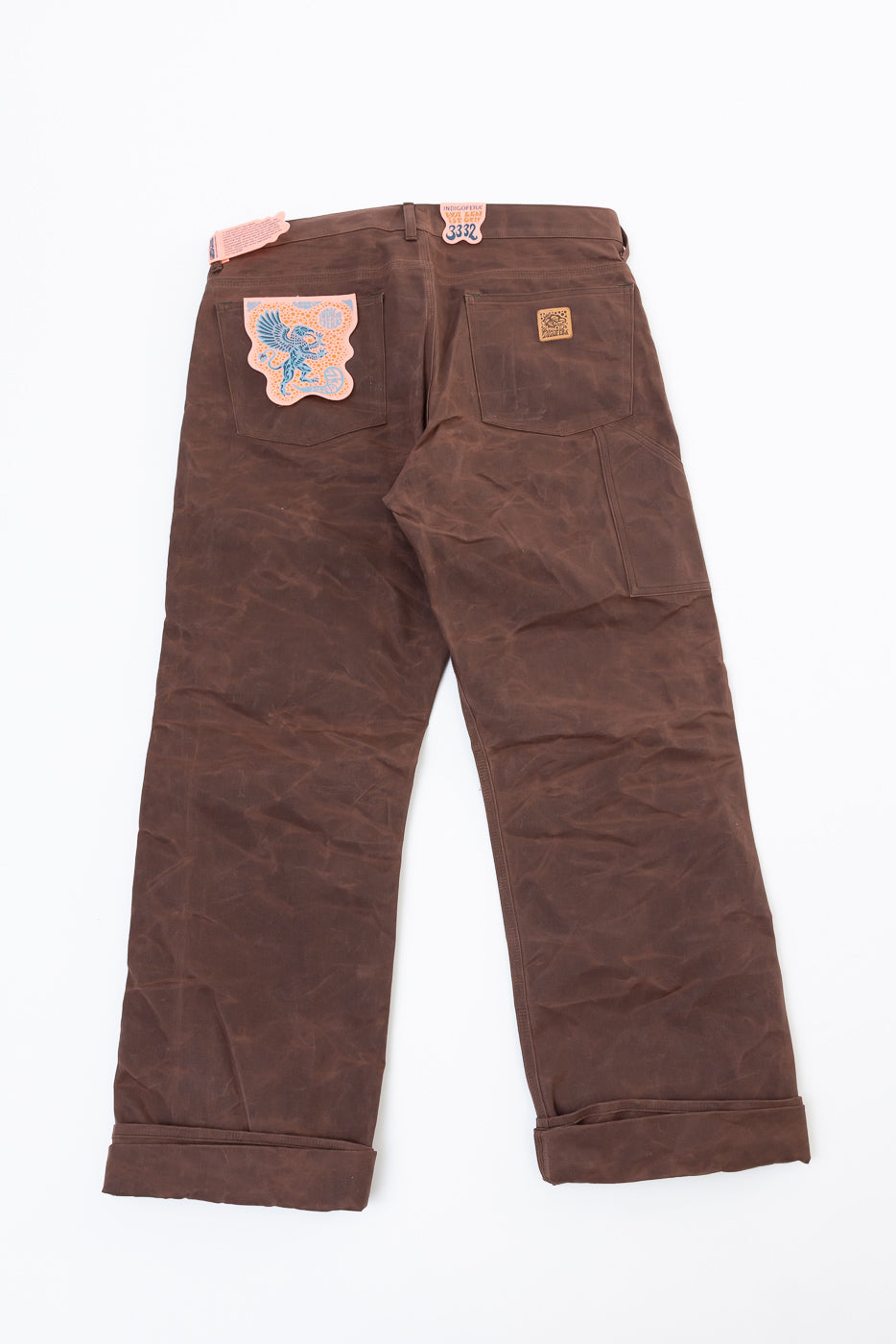 Flat lay of the back of brown wax canvas pants with a blue bird patch on the pocket.