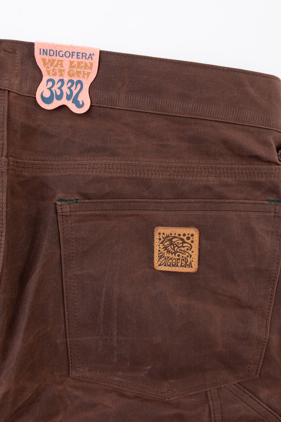 Close-up of the back pocket and waistband of brown Indigofera pants with a leather brand patch.