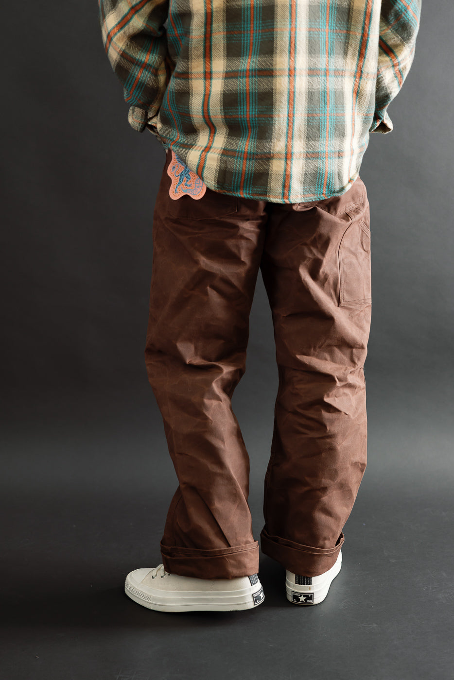 Back view of a male model wearing brown work pants and a plaid shirt.