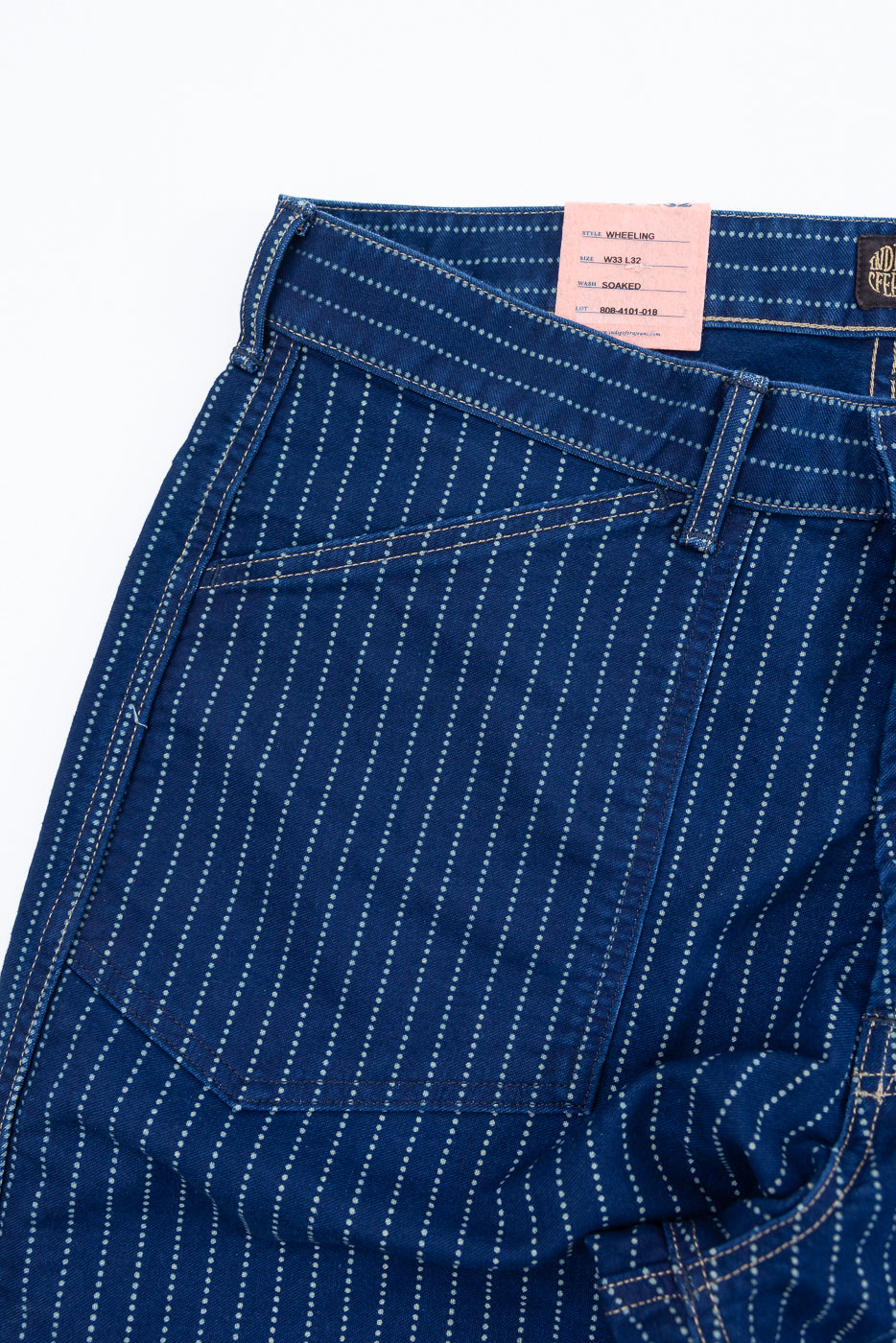 Close-up of the front waist and pocket of blue striped jeans showing a pink detail tag.
