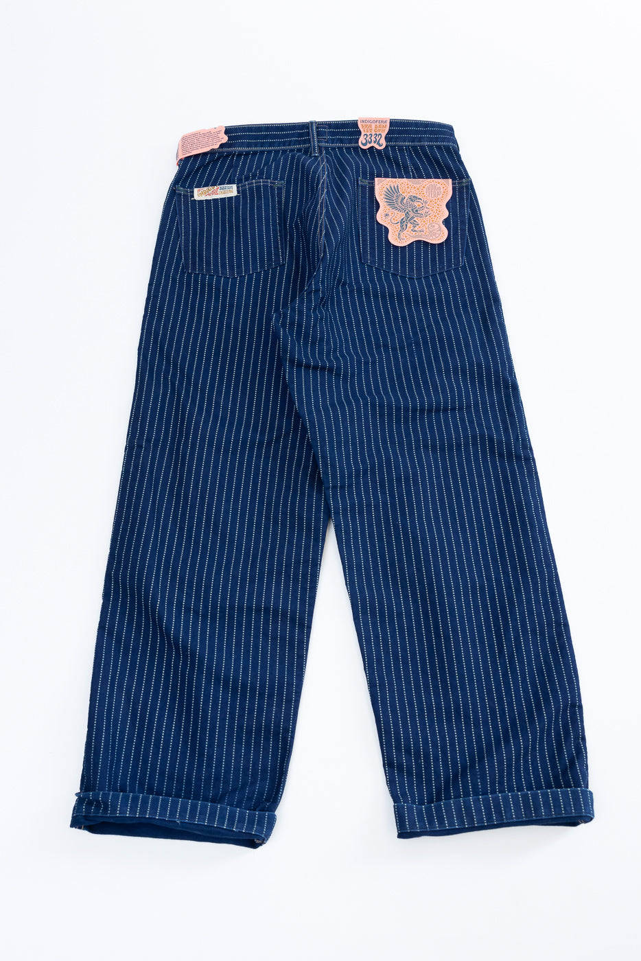 Back view flat lay of blue pinstripe pants featuring decorative patches and rolled hems.