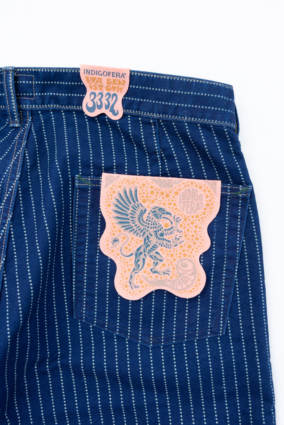 Close-up of the back of blue striped jeans featuring a waist tag and a griffin pocket patch.