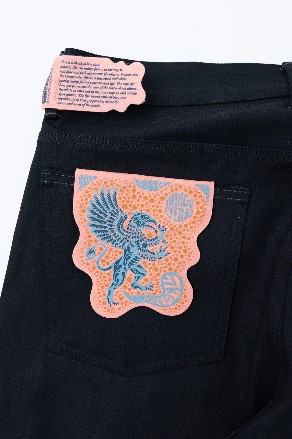 Close-up of black selvedge jeans back pocket with pink tag featuring blue griffin design and fabric details.
