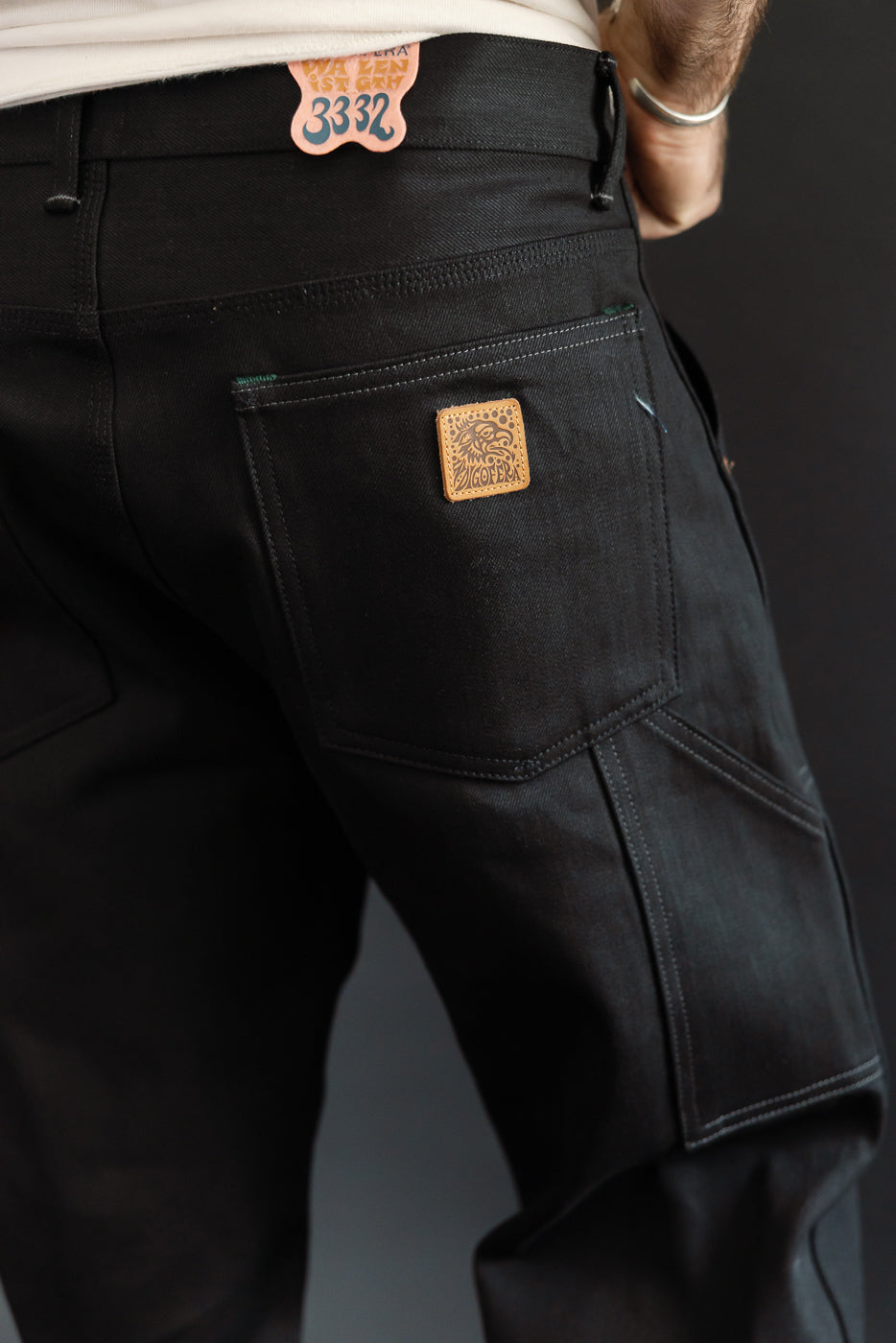 Close-up back view of black selvedge jeans with leather patch, worn by male model, 5'9
