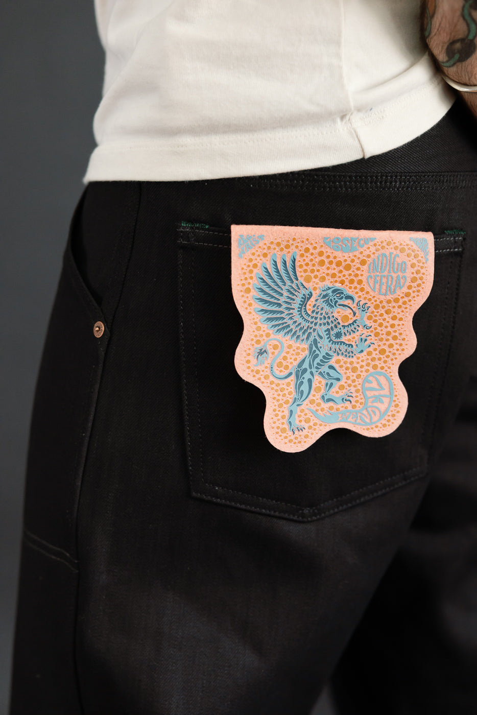 Close-up of black selvedge jeans back pocket with blue dragon patch, worn by male model.