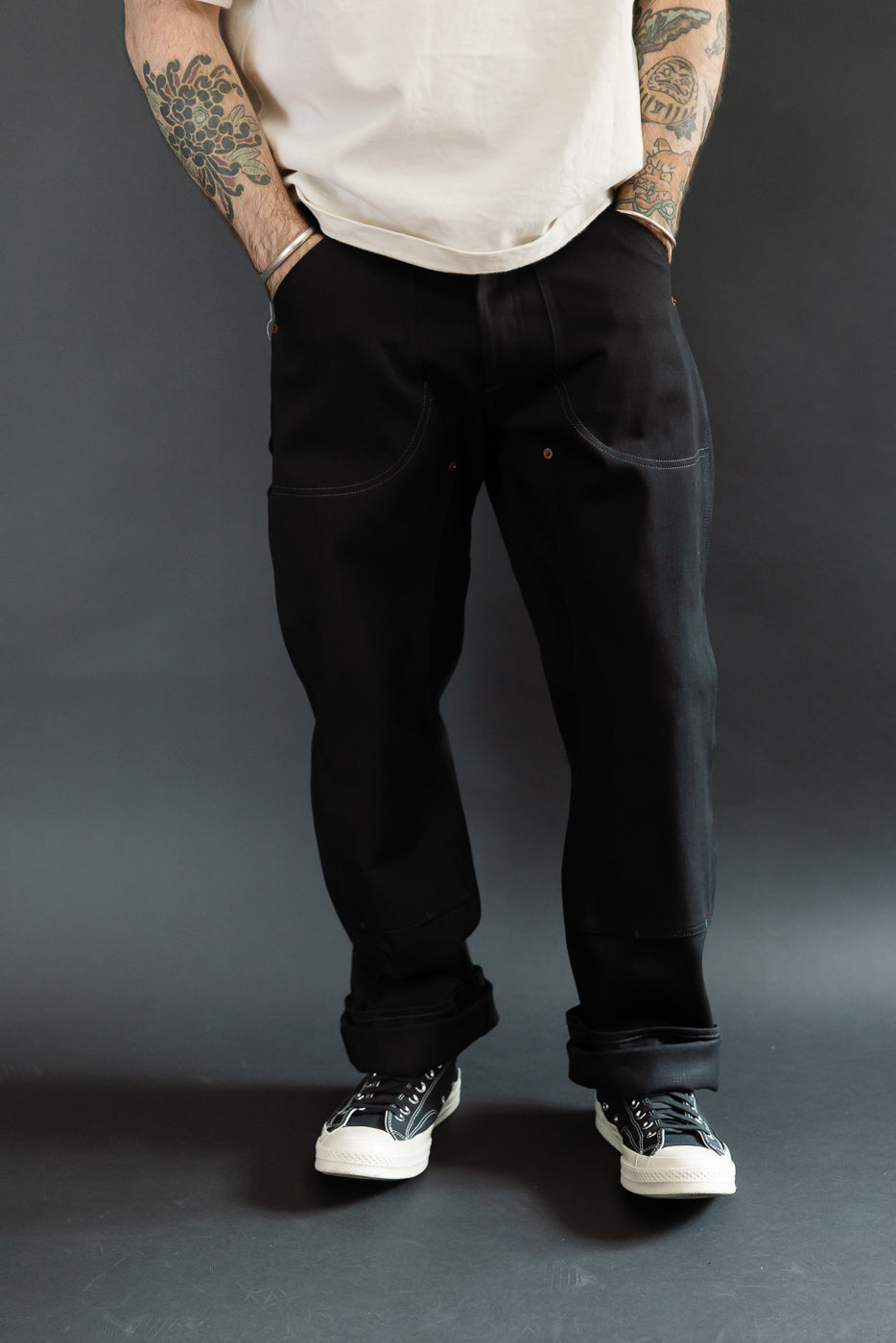 Full-body front view of male model in black selvedge work pants, cuffed hem, athletic build