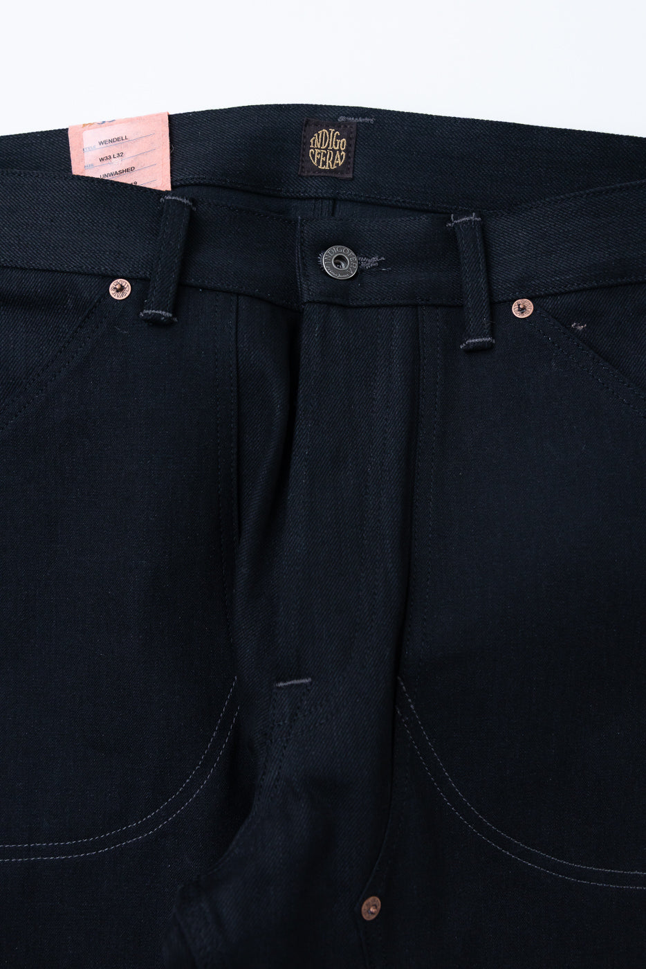 Front close-up of dark selvedge jeans, showing button fly, copper rivets, and brand tag details.