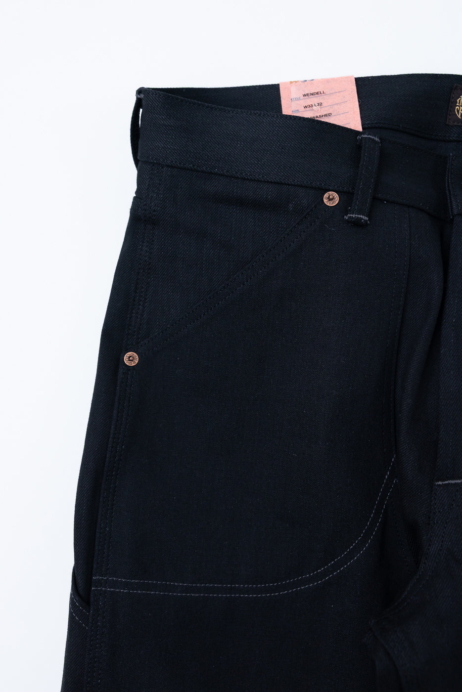 Close-up front view of dark selvedge jeans with copper buttons, white stitching, and waist tag detail