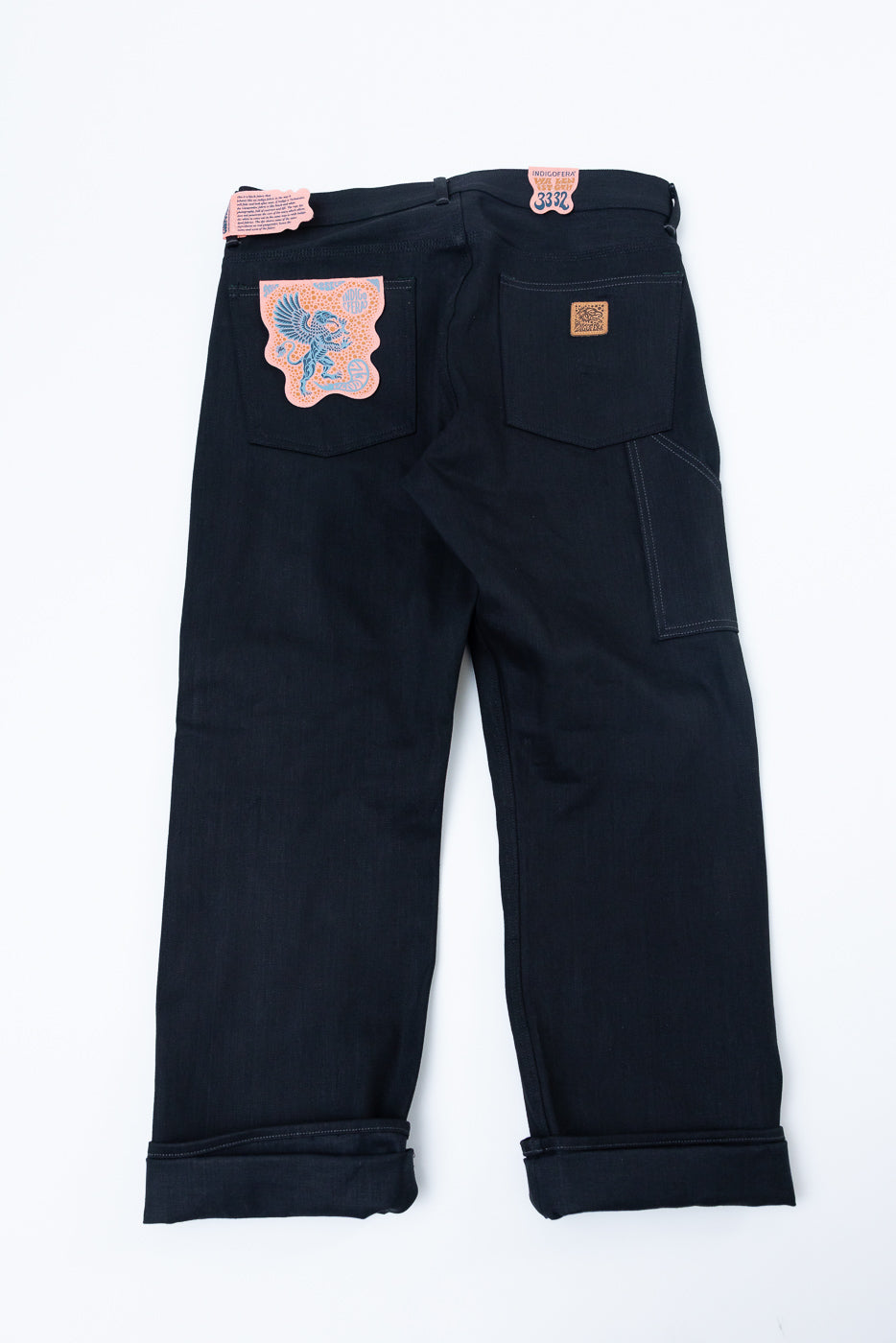 Back view of dark selvedge jeans with embroidered patch, cuffed hems, and side pocket detail
