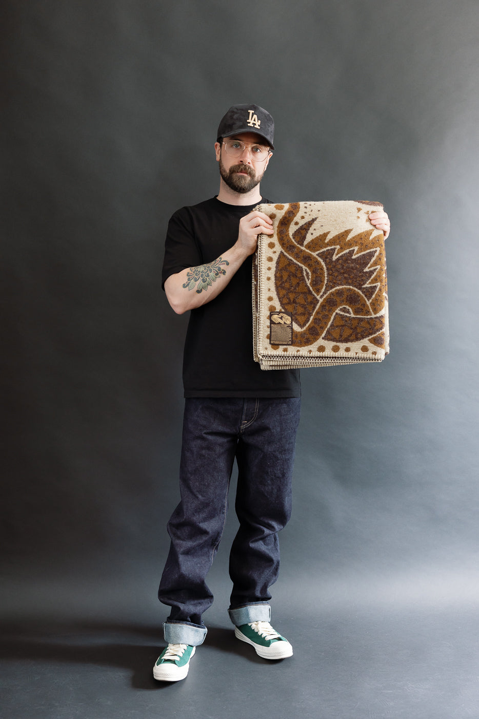 man holding folded brown and beige blanket on a white background with custom artwork tag in lower left corner