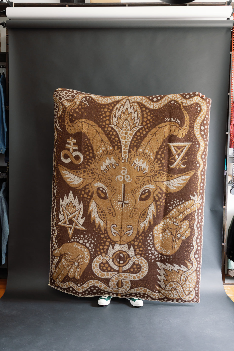 fully open brown and beige blanket on a black background with custom artwork of baphomet, hands, serpent, and other sigils, back side