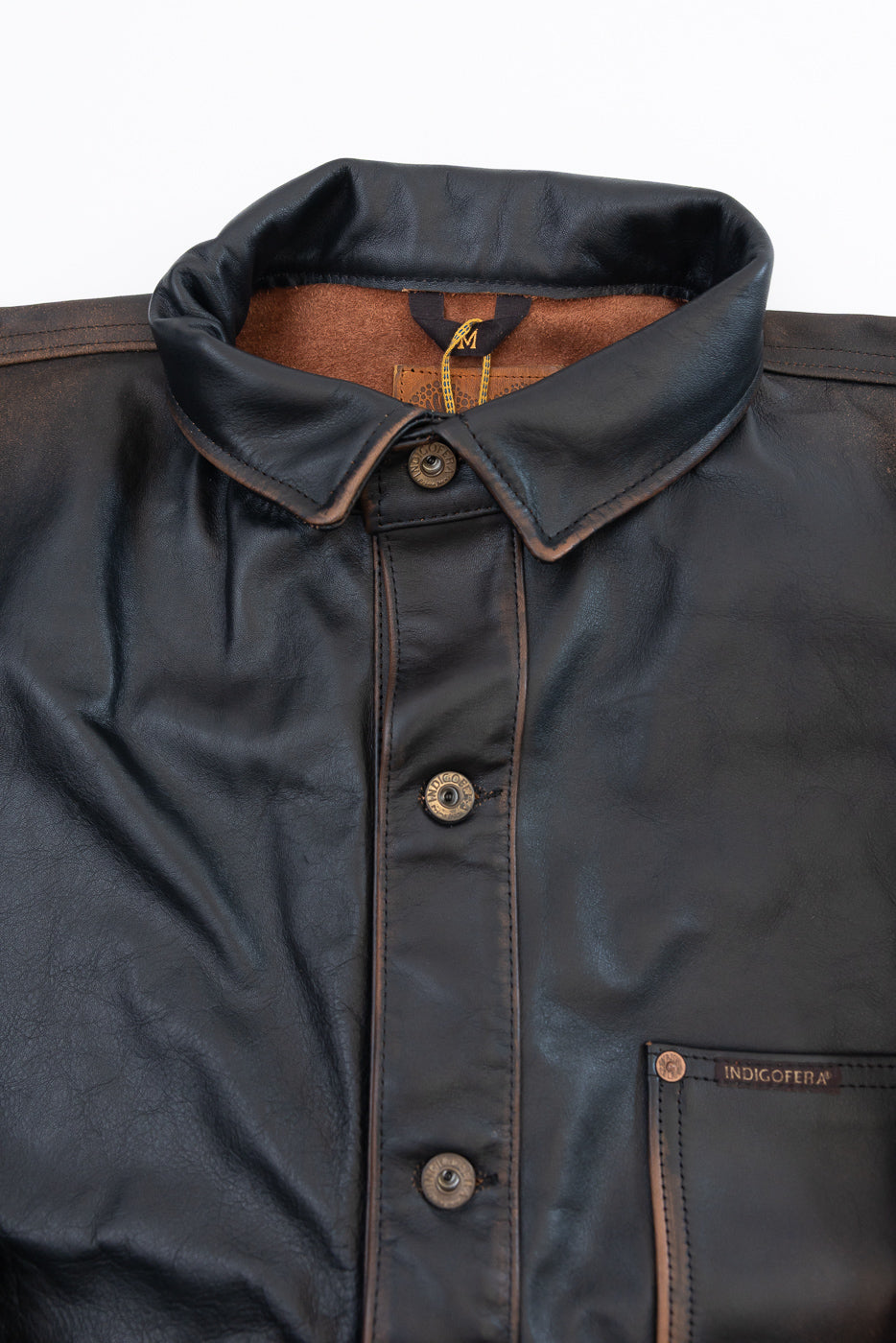 Close-up of the front collar and chest of a dark brown leather jacket with buttons and tag.