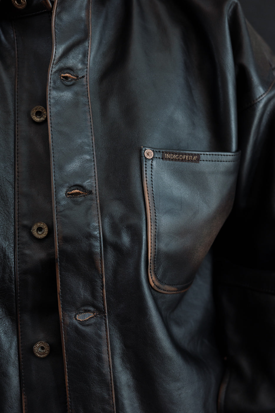 Close-up of the front of a black leather jacket showing a chest pocket and buttons.