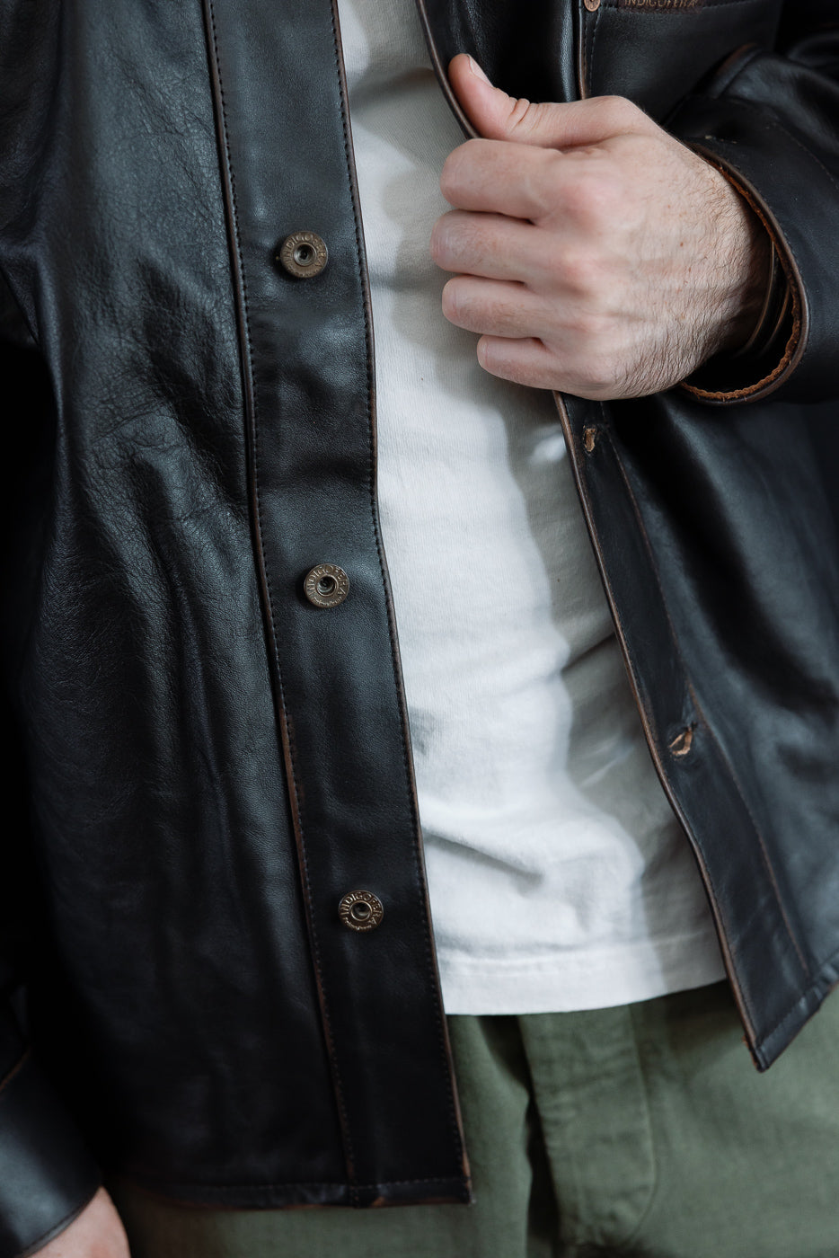 Close-up front view of a black leather jacket with bronze buttons on a 5'9