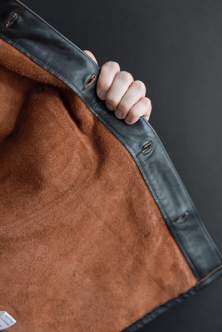 Close-up of the interior brown suede lining and black leather edge of a garment.