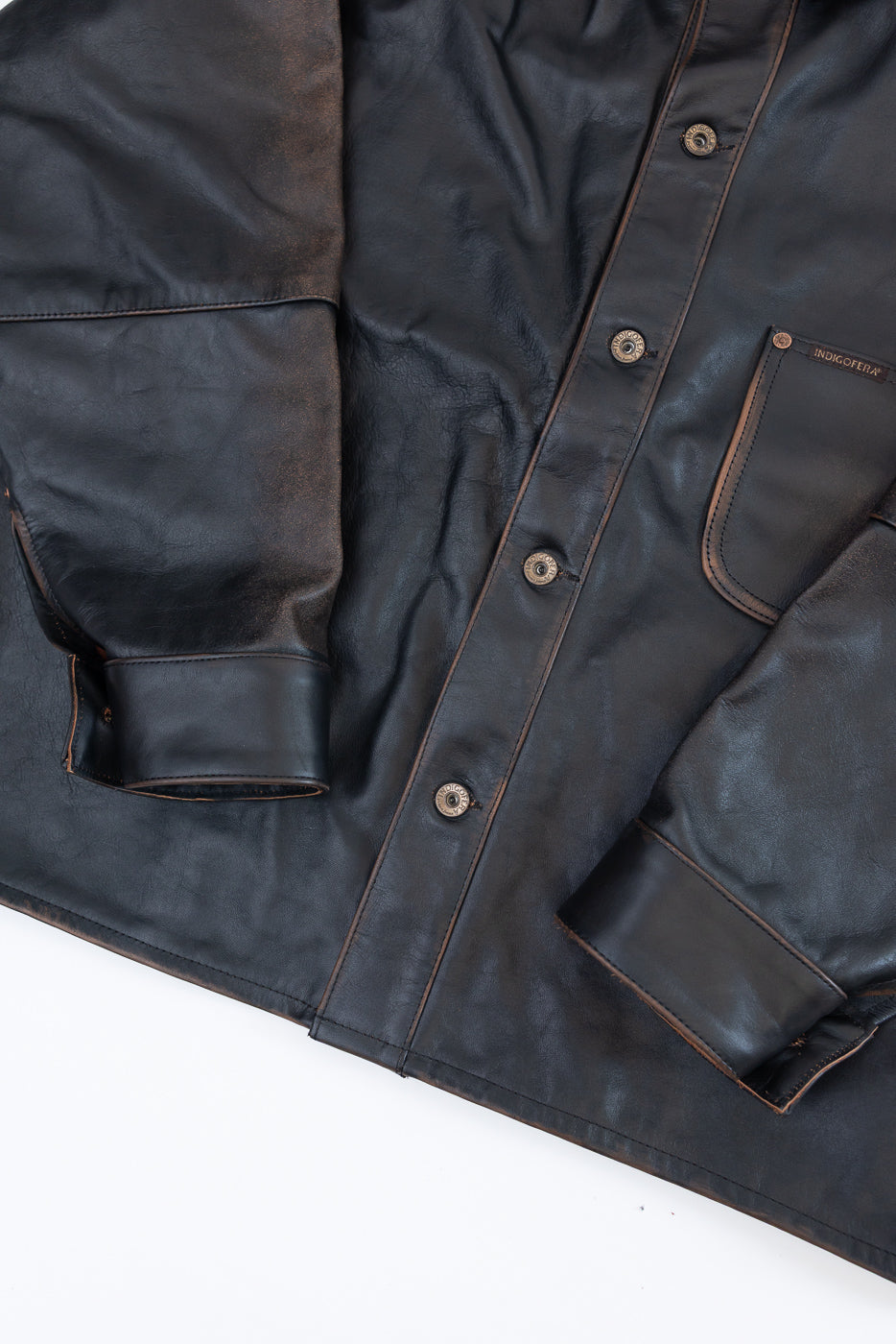 Close-up of the front of a dark brown leather shirt showing buttons and chest pocket.