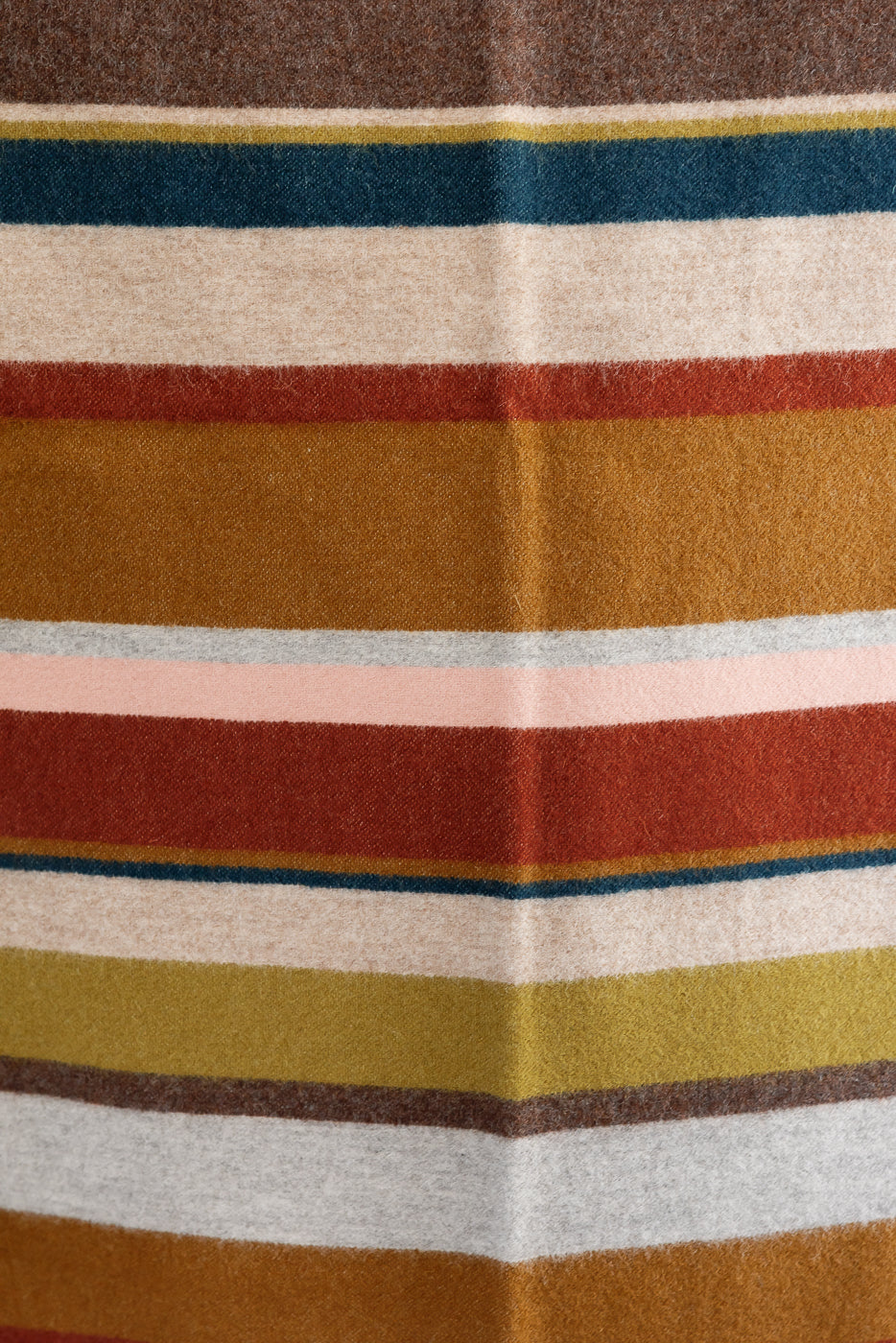 close up of wool striped blanket against black background, stripes of pink, clay, mustard, brown, grey, beige, and navy in different varying widths