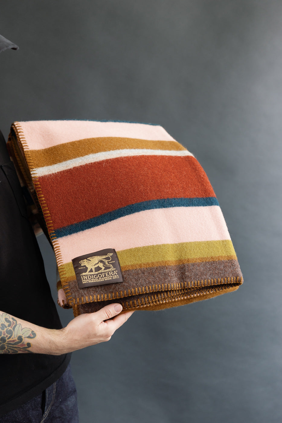 Person holding a striped blanket with a brand logo against a black background