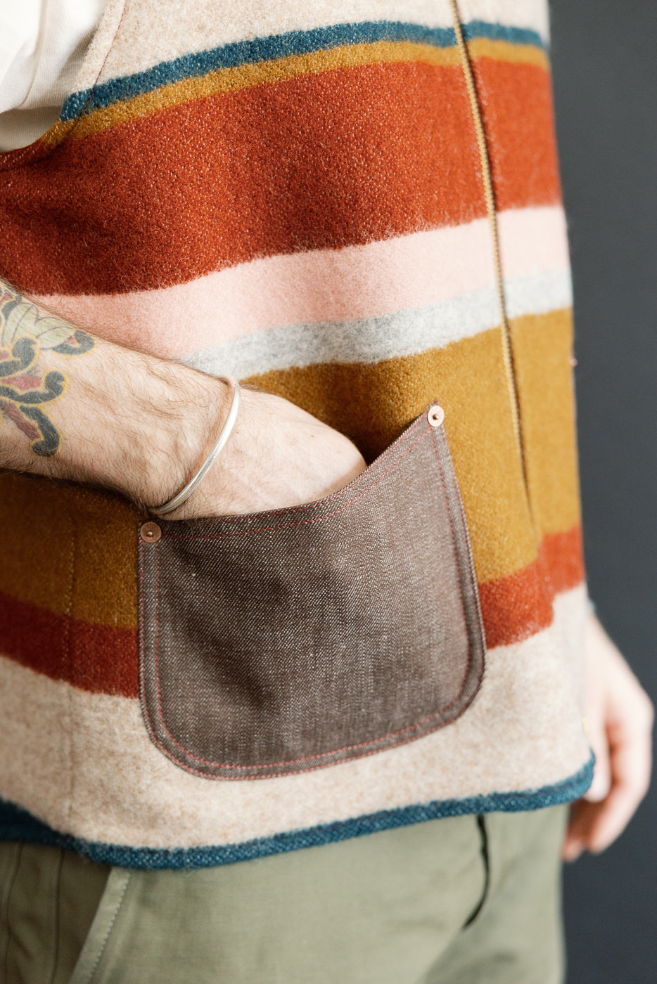 Close-up of male model's side pocket on striped wool vest, showcasing texture and stitching detail.