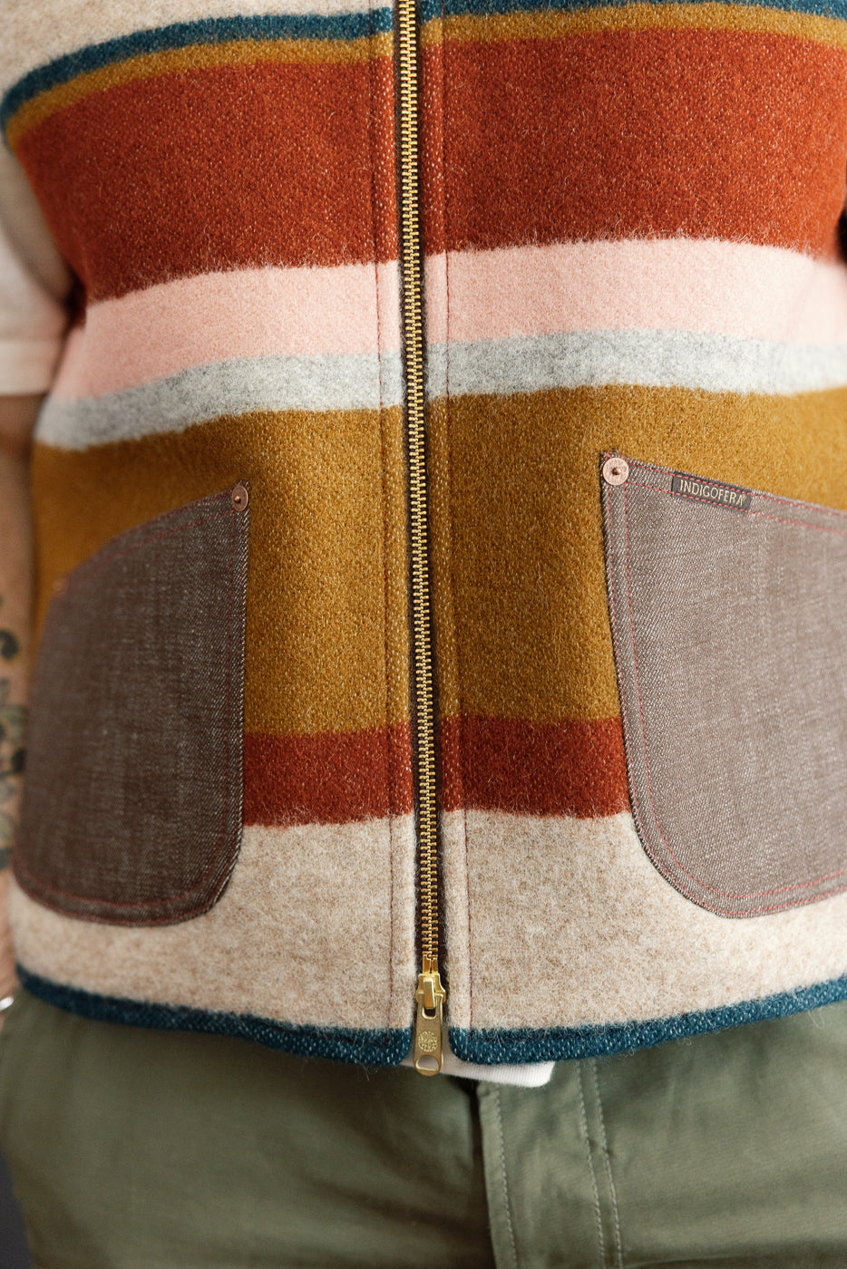 Close-up front view of striped wool jacket with gold zipper, patch pockets, and Indigofera tag, worn by male model.