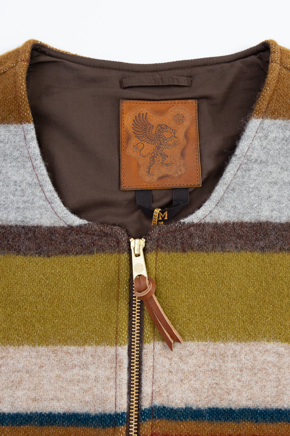 Close-up front view of striped wool vest showing leather brand patch, gold zipper, and leather pull tab
