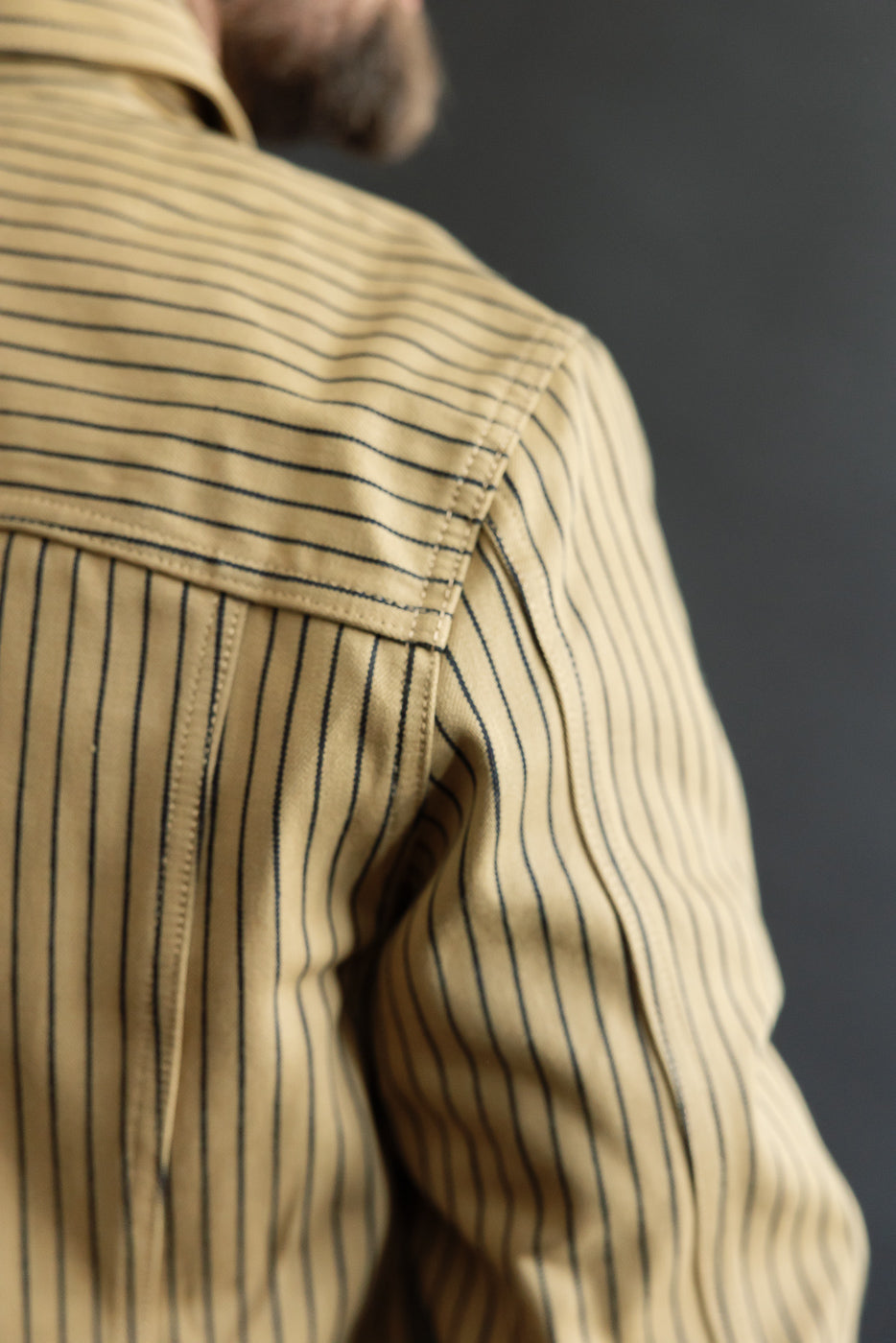 Close-up of back shoulder detail on beige indigo striped shirt, male model, right side.