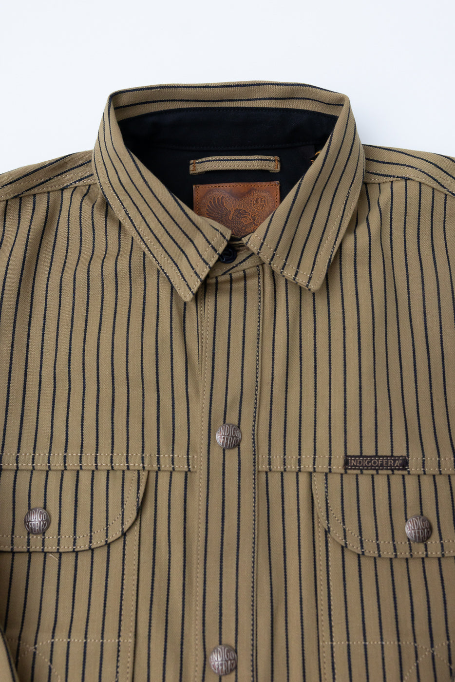 Close-up front of beige and indigo striped shirt jacket, showing collar, chest pockets, metal snaps, and textured fabric.